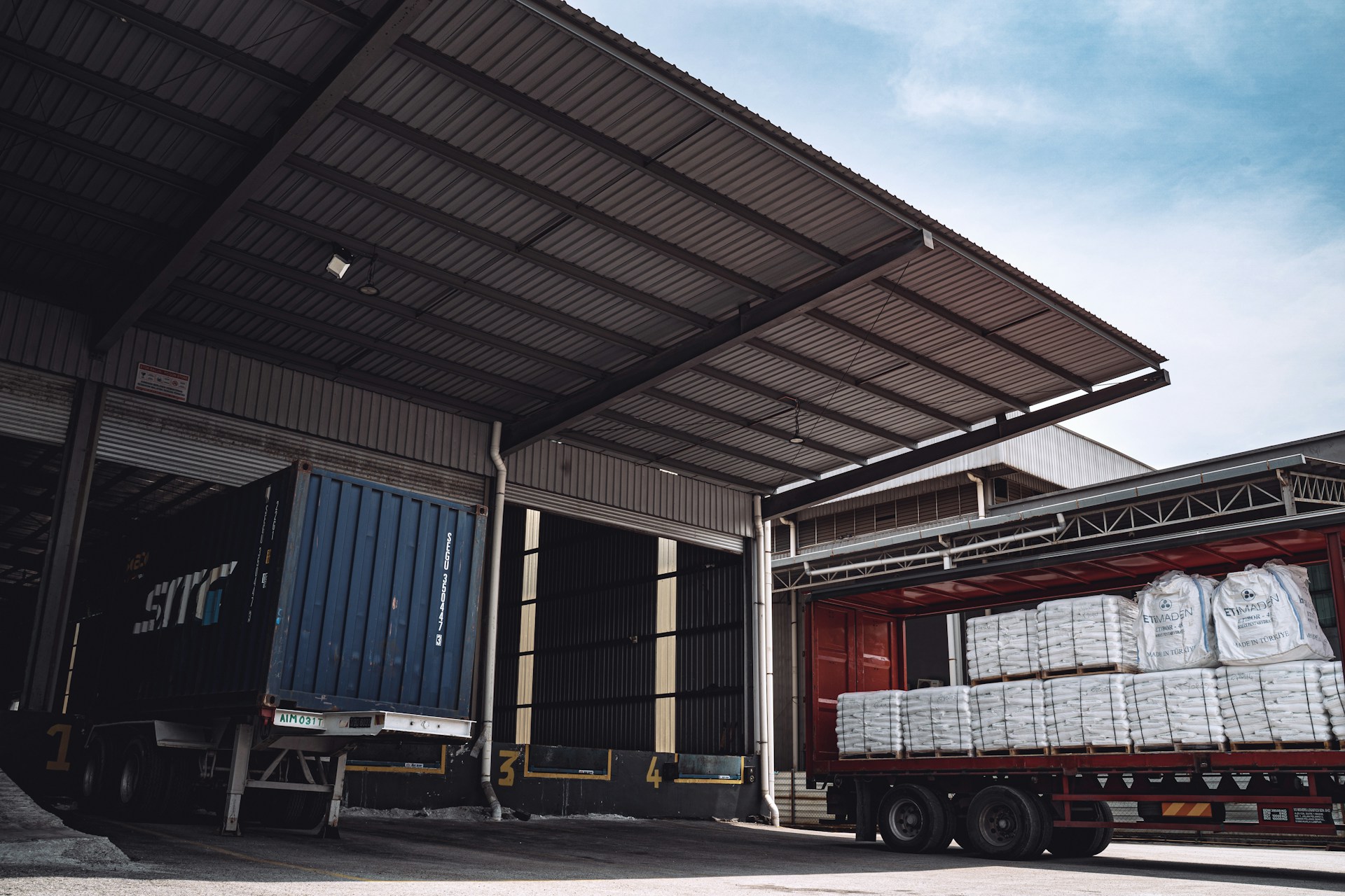Semi-trailer and shipping container at a warehouse loading bay with palletised goods