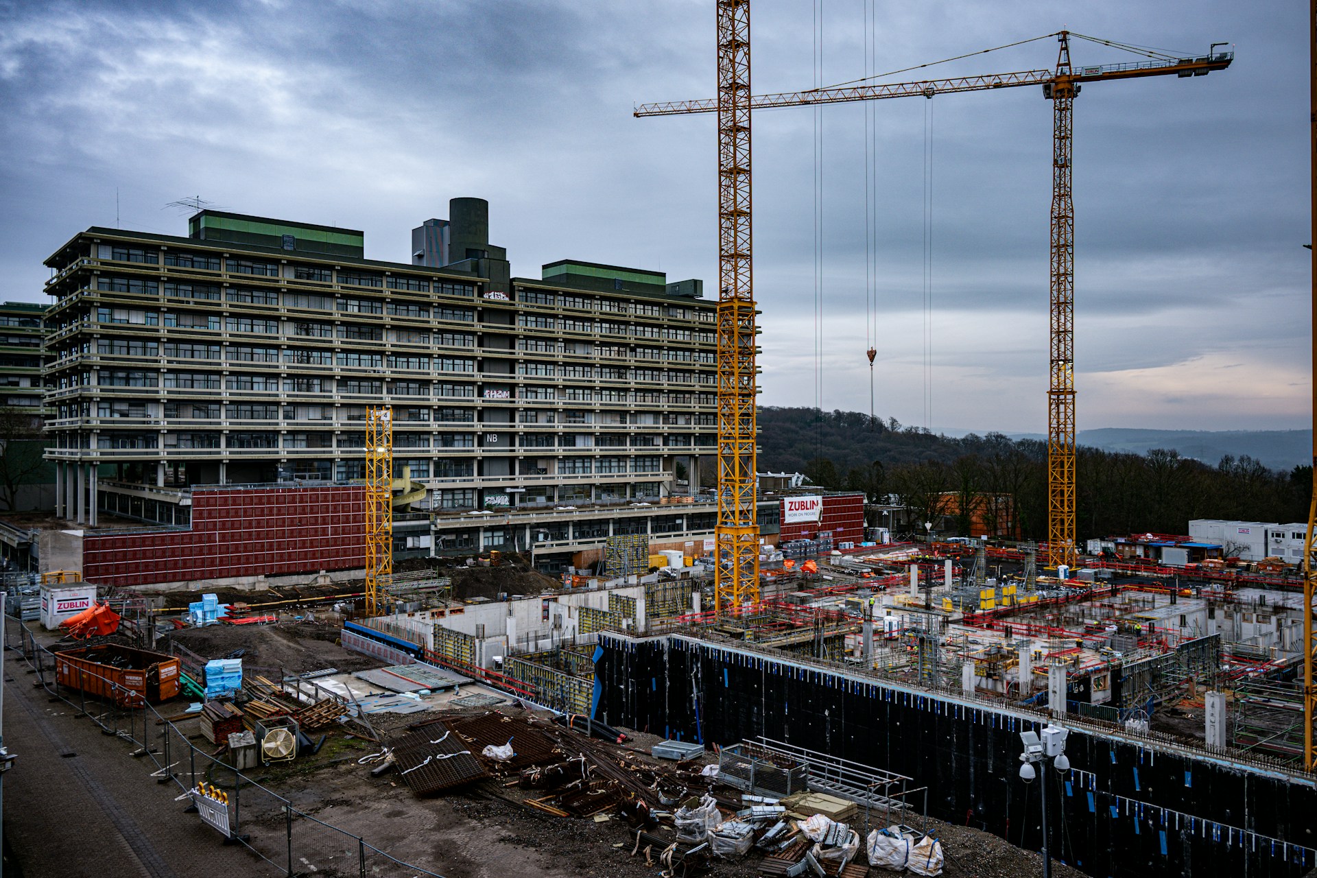 Large city construction site at dusk with tower cranes and perimeter fencing